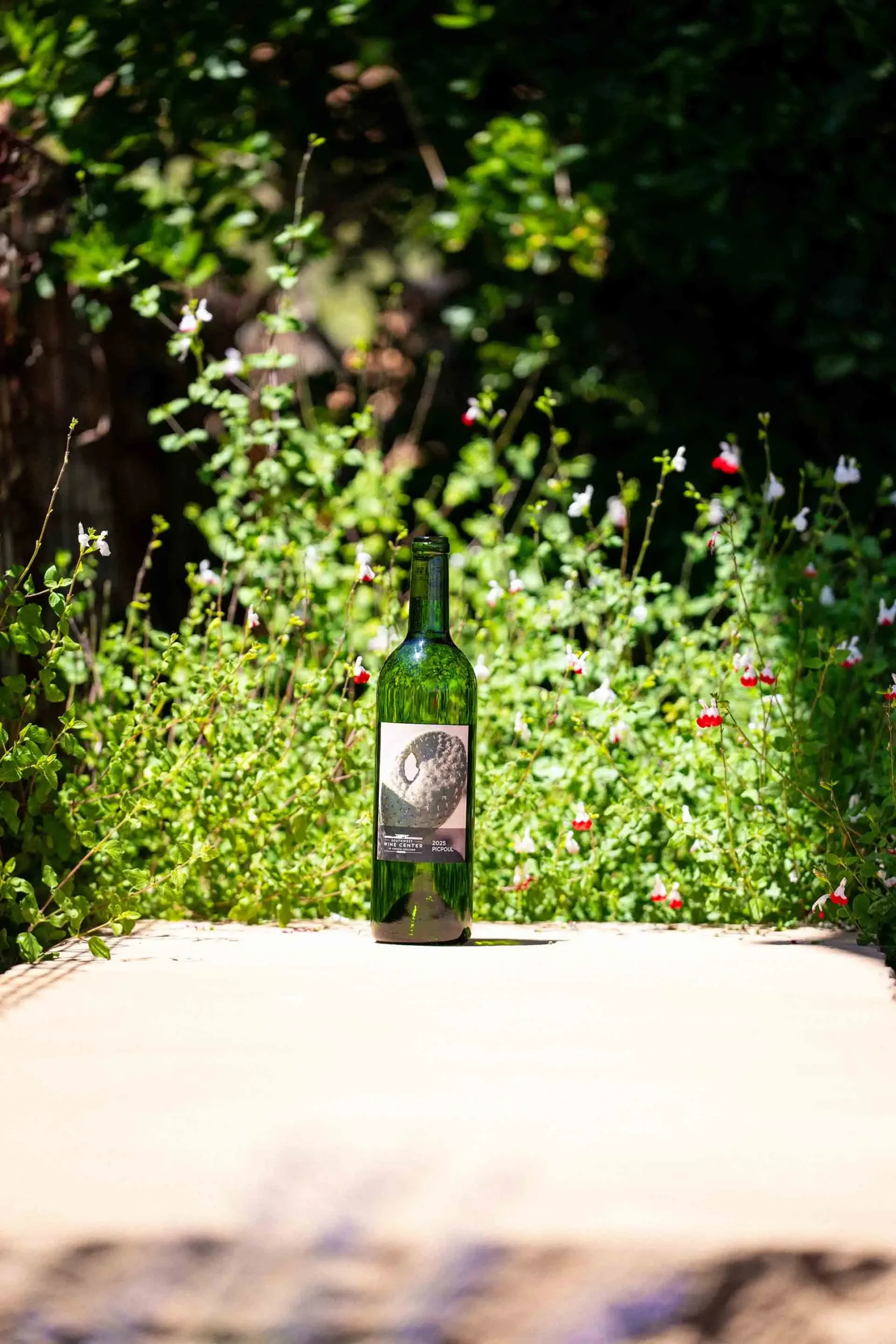 Bottle of Southwest Wine Center wine displayed outdoors in a garden with wildflowers and natural sunlight
