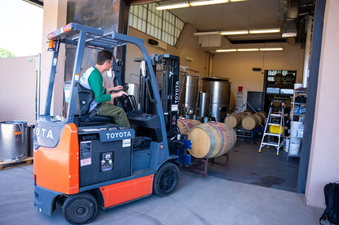 Winery worker moving a wine barrel by forklift, illustrating what is enology